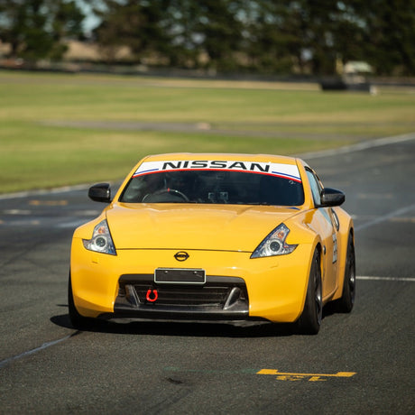 Yellow Nissan sports car on a track with grass and trees in the background